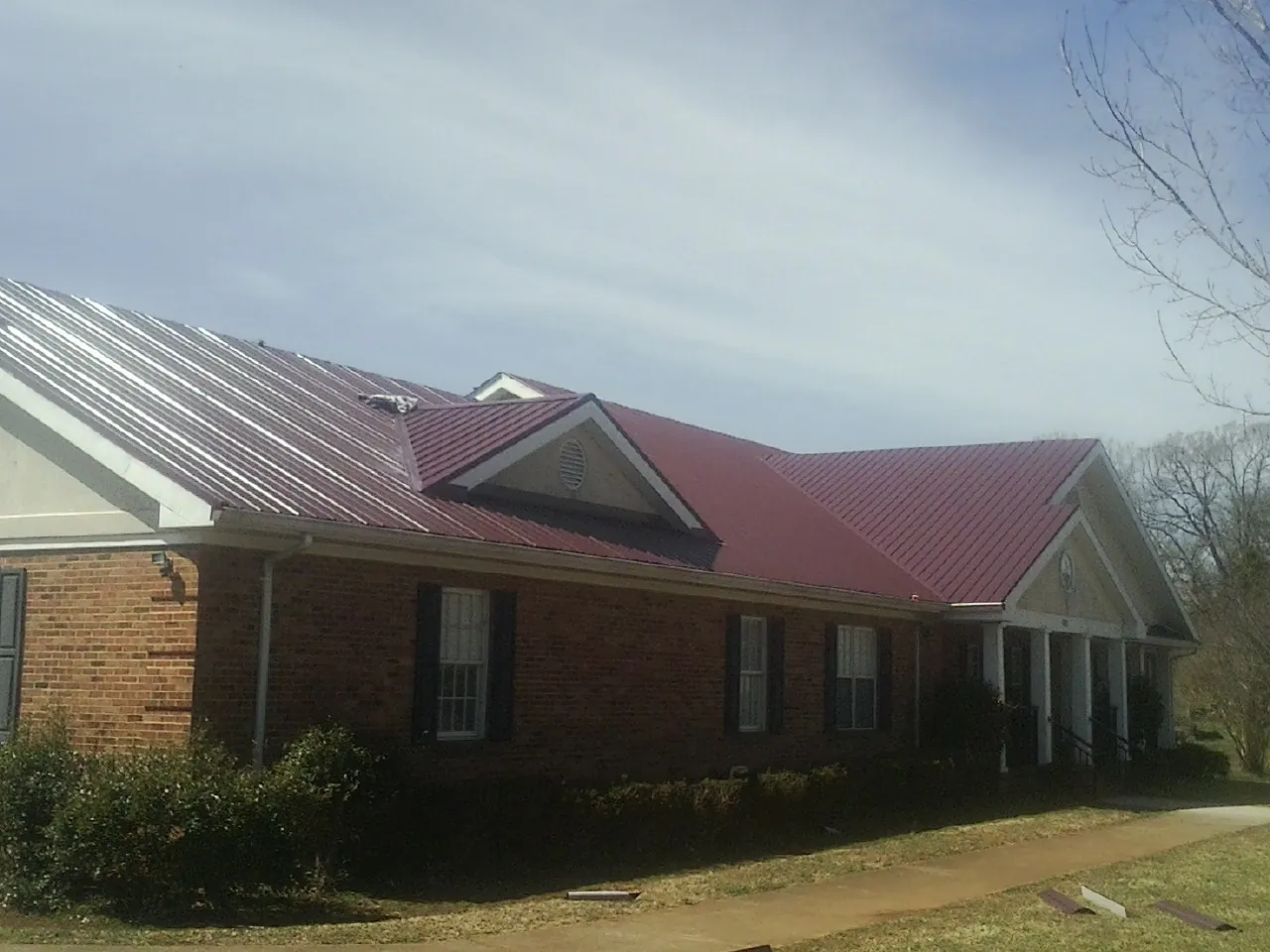 Red metal roof with gabled entries on a long brick building, from a Hail Damage Roof Repair job in Apache
