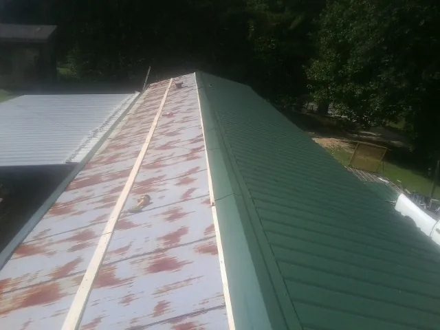Old rusted panels beside newly installed green metal roofing — Wind Damage Roof Repair by Roofing Brothers in Apache