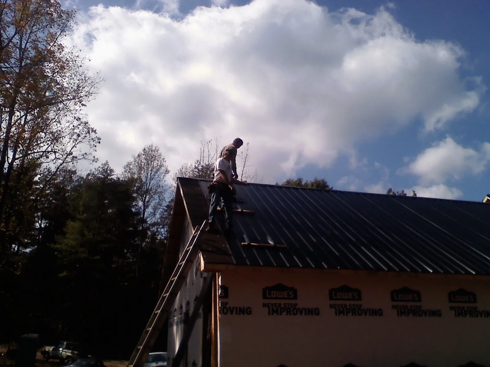 Roofer fastening dark metal panels high against a cloudy sky, from a Roof Inspection job in Apache