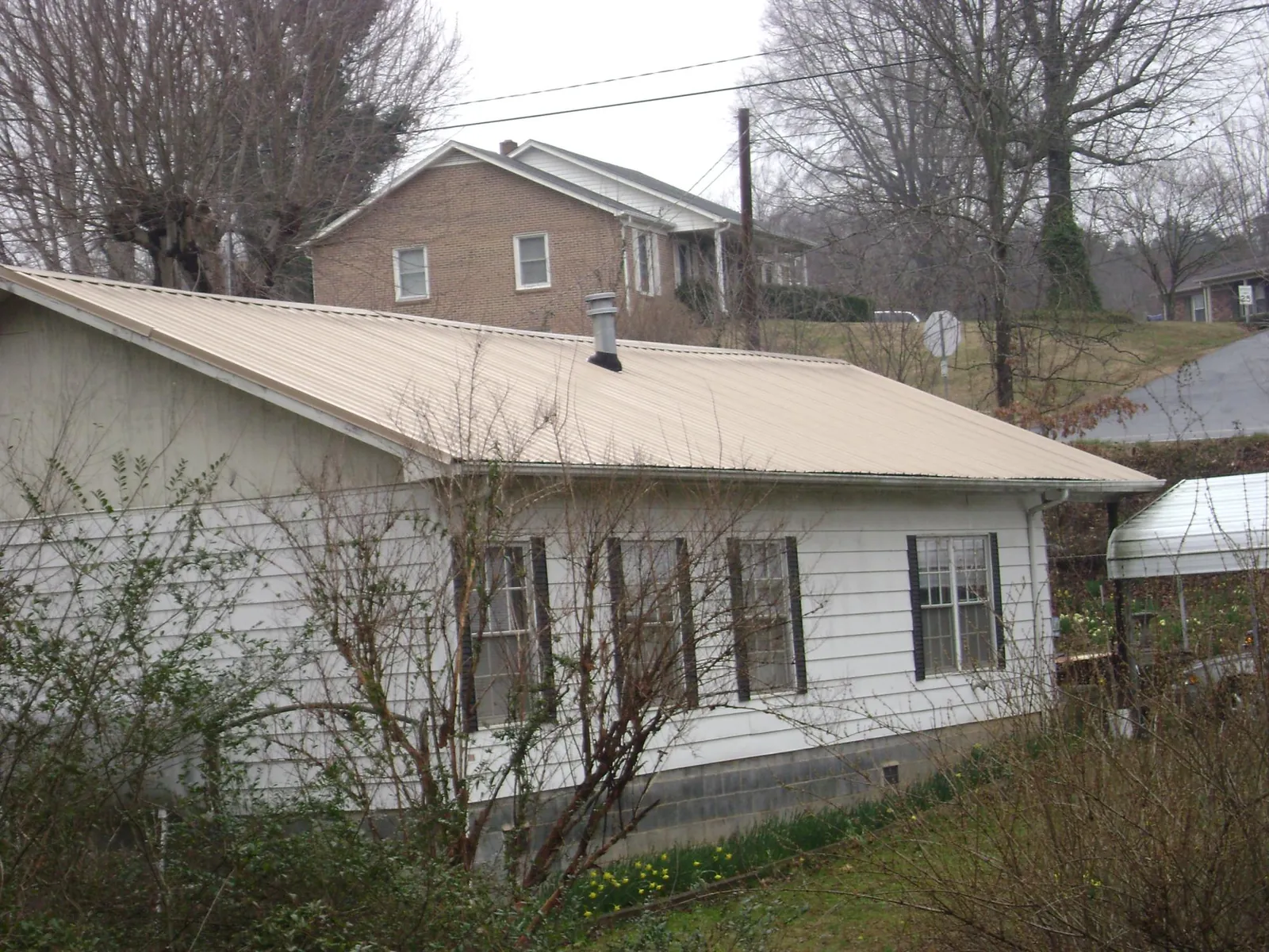 Tan metal roof on a white sided house set into a hillside — Commercial Roofing by Roofing Brothers in Apache